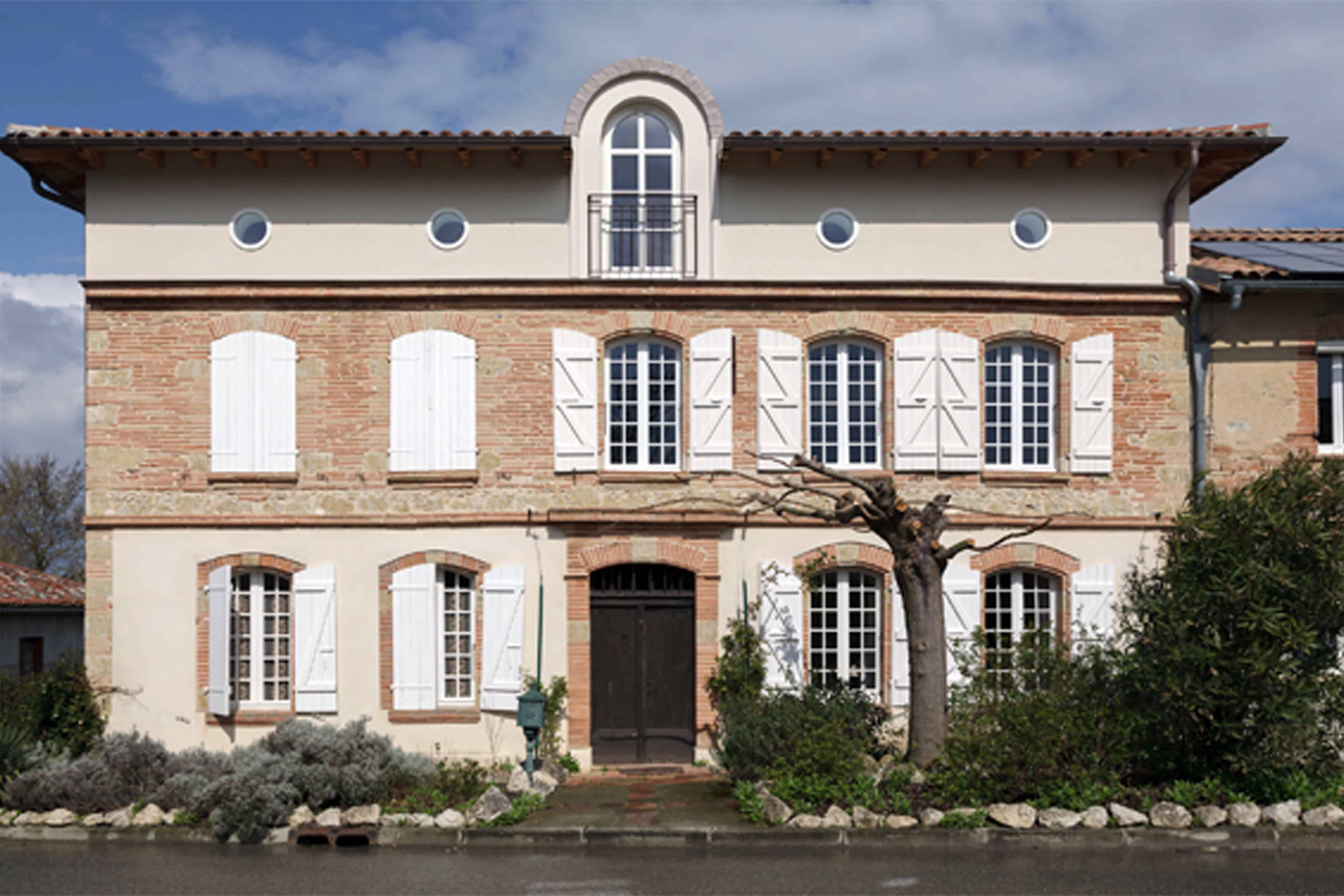 Façade ordonnancée d'une maison de village en briques et enduit, surélevée d'un niveau coiffé d'œils-de-bœuf et d'une lucarne cintrée en zinc rouge